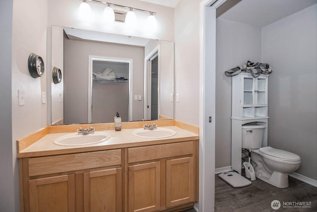 bathroom with toilet, wood finished floors, double vanity, and baseboards
