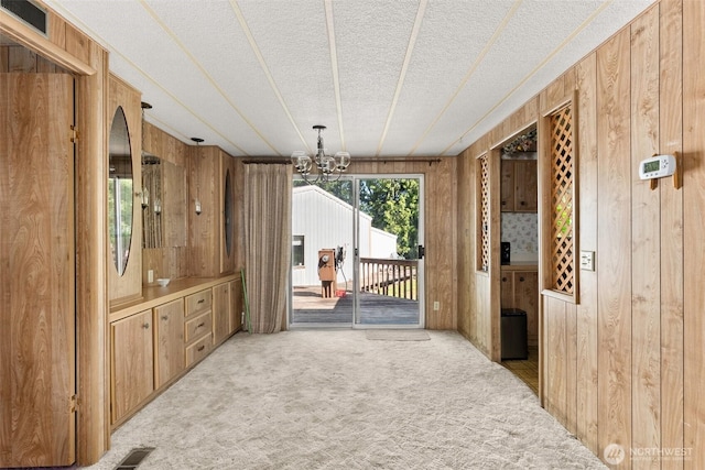 unfurnished dining area featuring wooden walls, light colored carpet, a textured ceiling, and a chandelier