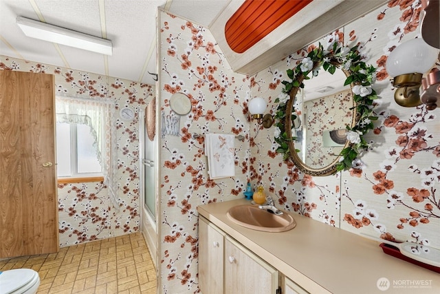 bathroom with wallpapered walls, vanity, toilet, and combined bath / shower with glass door
