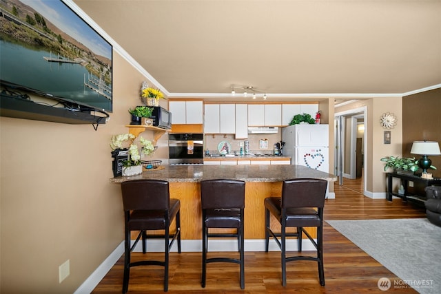 kitchen with a peninsula, oven, under cabinet range hood, crown molding, and backsplash