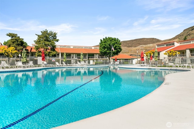 community pool featuring fence, a mountain view, and a patio