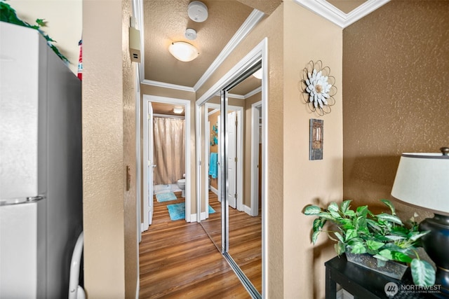 hall with wood finished floors, ornamental molding, and baseboards