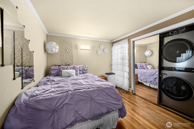 bedroom with stacked washer / drying machine, wood finished floors, and crown molding