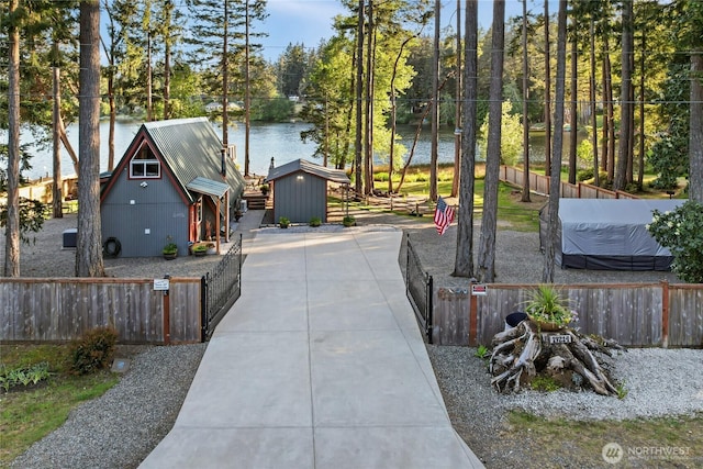 fenced yard featuring a water view, an outdoor structure, a storage shed, and view of scattered trees