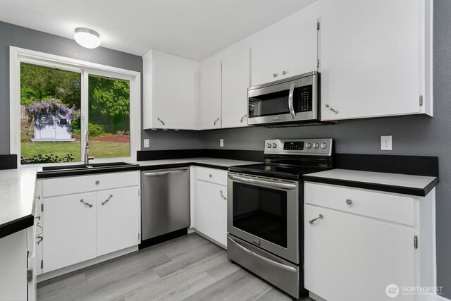 15221 42nd Ave E, Tacoma, WA 98446 - kitchen featuring stainless steel appliances, a sink, dark countertops, light wood-style flooring, and white cabinetry
