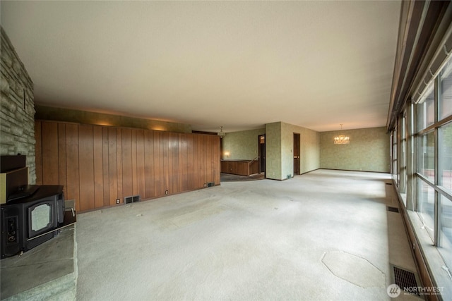 906 E 3rd Ave, Ellensburg, WA 98926 - unfurnished living room with a wood stove, wood walls, a chandelier, and light carpet