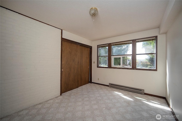 906 E 3rd Ave, Ellensburg, WA 98926 - unfurnished bedroom featuring a baseboard heating unit, light colored carpet, a closet, brick wall, and baseboards