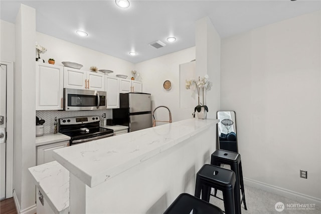 kitchen with stainless steel appliances, a peninsula, a kitchen bar, white cabinets, and backsplash