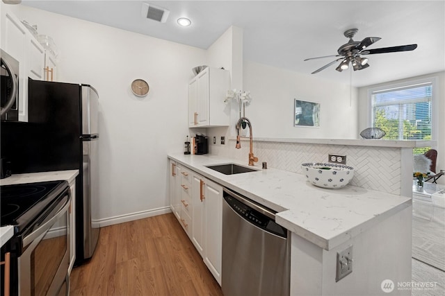 kitchen with stainless steel appliances, a sink, a peninsula, backsplash, and white cabinets