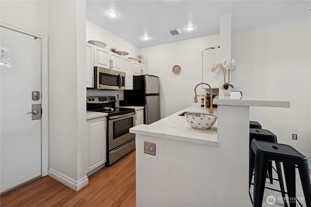 kitchen with stainless steel appliances, a kitchen bar, light wood-style flooring, white cabinetry, and a sink