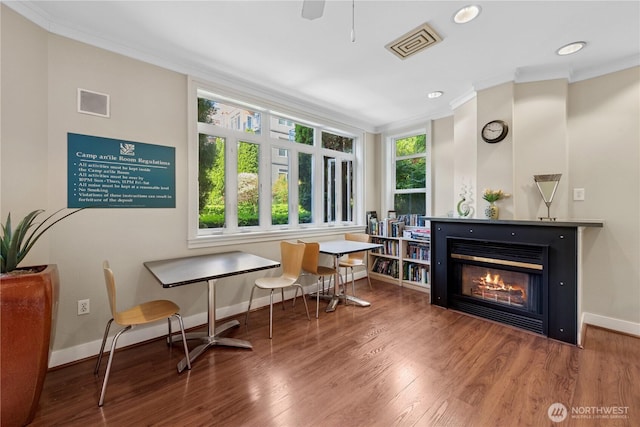 sitting room with ornamental molding, baseboards, wood finished floors, recessed lighting, and a glass covered fireplace