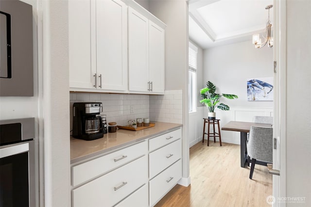 kitchen with light wood finished floors, decorative backsplash, light countertops, white cabinetry, and decorative light fixtures