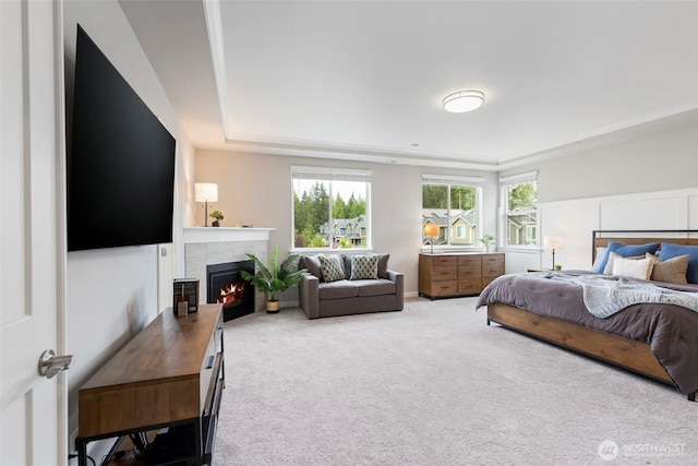 bedroom featuring a raised ceiling, multiple windows, a warm lit fireplace, and carpet flooring