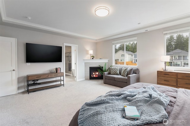 bedroom featuring a raised ceiling, a glass covered fireplace, and carpet floors