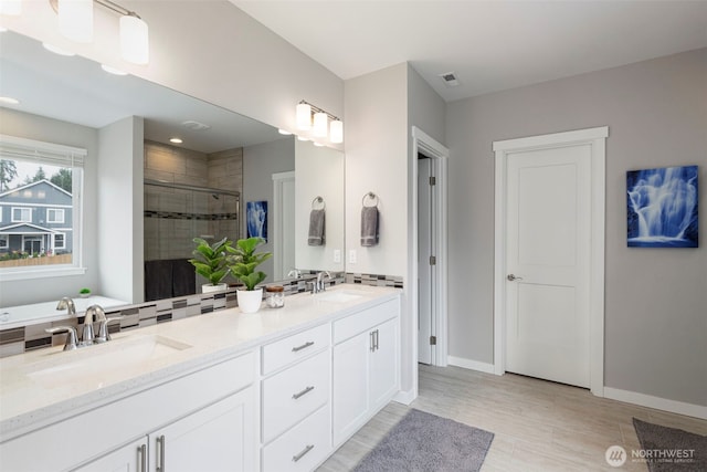 full bathroom with a stall shower, wood finished floors, double vanity, and baseboards