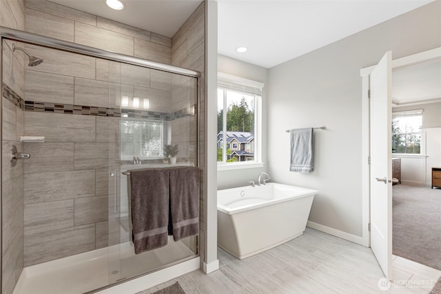 bathroom featuring baseboards, a shower stall, a freestanding tub, plenty of natural light, and recessed lighting