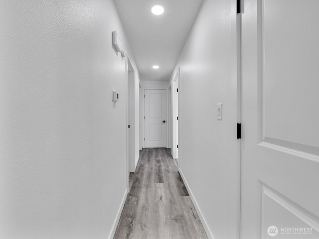 corridor with light wood finished floors, baseboards, and recessed lighting