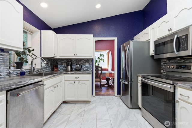 kitchen featuring appliances with stainless steel finishes, lofted ceiling, white cabinetry, a sink, and recessed lighting