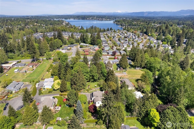 aerial view of property and surrounding area featuring a water and mountain view and a forest