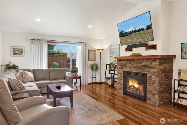 living area with baseboards, wood finished floors, lofted ceiling, and a stone fireplace
