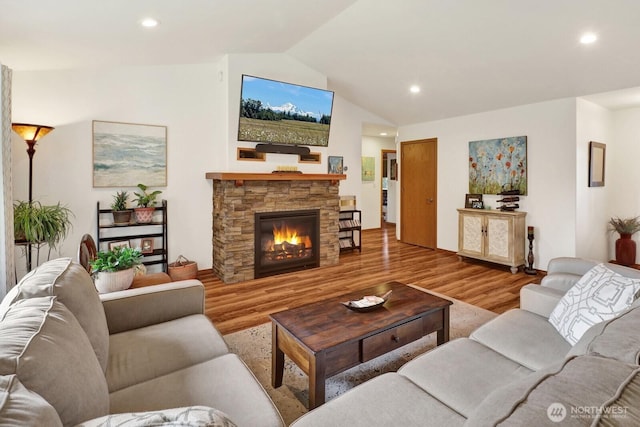living area featuring wood finished floors, lofted ceiling, a stone fireplace, and recessed lighting