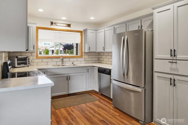 kitchen with wood finished floors, a sink, backsplash, light countertops, and appliances with stainless steel finishes