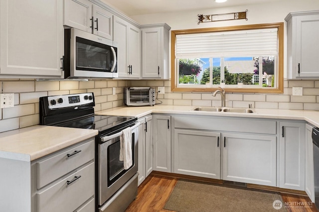 kitchen with stainless steel appliances, a toaster, a sink, decorative backsplash, and light countertops