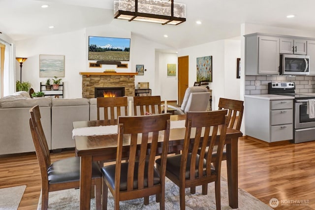 dining area featuring light wood-type flooring, a fireplace, lofted ceiling, and recessed lighting