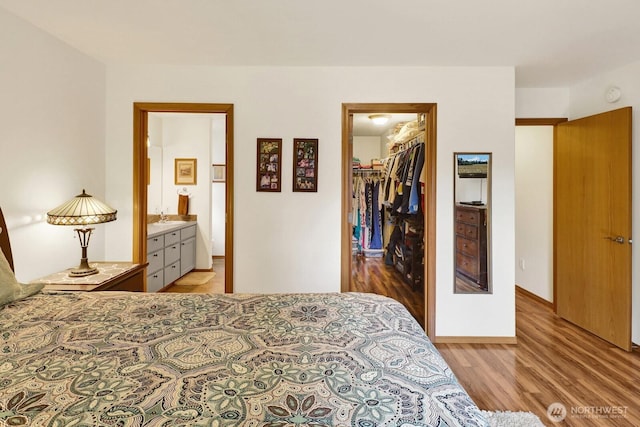 bedroom with light wood-style flooring, a sink, a closet, ensuite bath, and a spacious closet