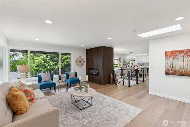 living room featuring a skylight, light wood-type flooring, recessed lighting, and baseboards