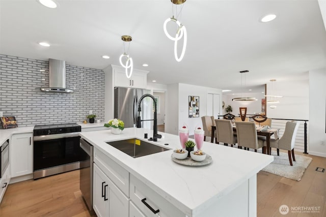 kitchen featuring wall chimney exhaust hood, appliances with stainless steel finishes, a sink, hanging light fixtures, and recessed lighting
