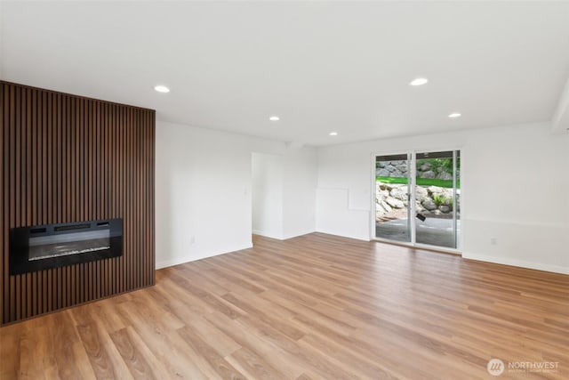 unfurnished living room with wood finished floors, recessed lighting, baseboards, and a glass covered fireplace