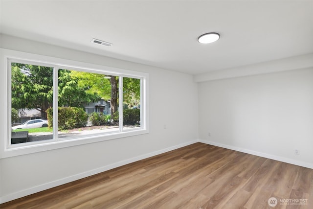 spare room with healthy amount of natural light, baseboards, and wood finished floors