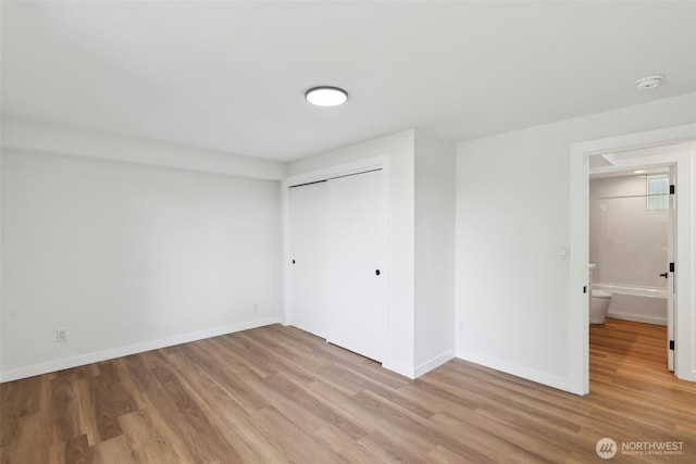 unfurnished bedroom featuring light wood finished floors, baseboards, and a closet