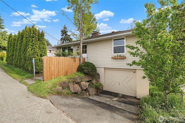 view of side of home featuring an attached garage, fence, a chimney, and driveway