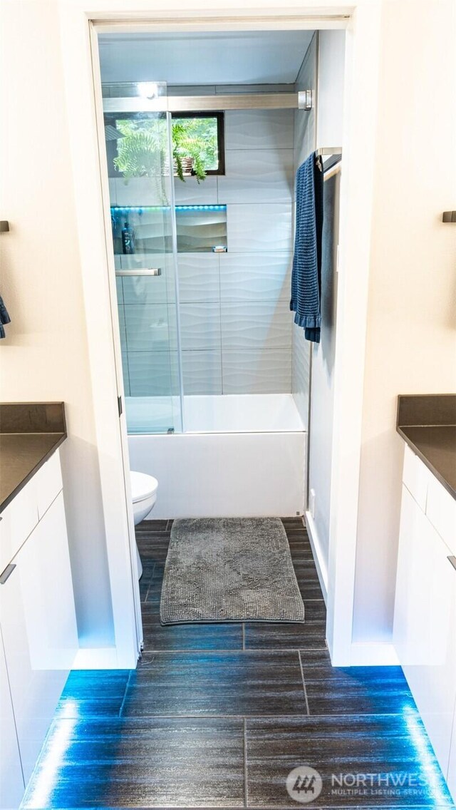 full bathroom featuring vanity, toilet, bath / shower combo with glass door, and baseboards