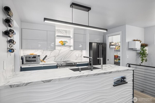 kitchen with appliances with stainless steel finishes, a sink, modern cabinets, backsplash, and light stone counters