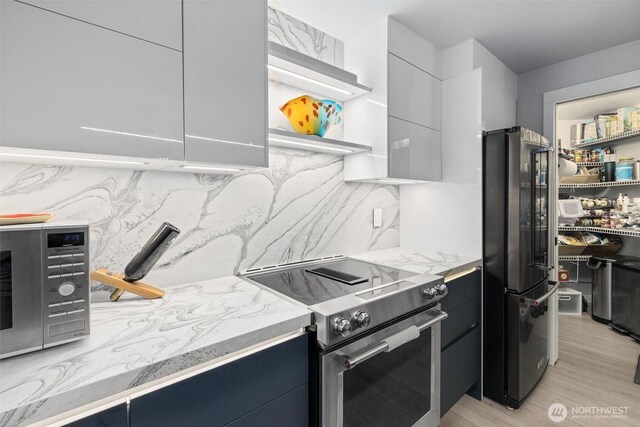 kitchen featuring premium appliances, tasteful backsplash, light wood-style floors, and modern cabinets
