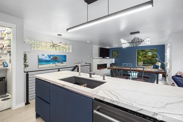 kitchen featuring a sink, stainless steel dishwasher, light stone counters, a fireplace, and light wood-type flooring