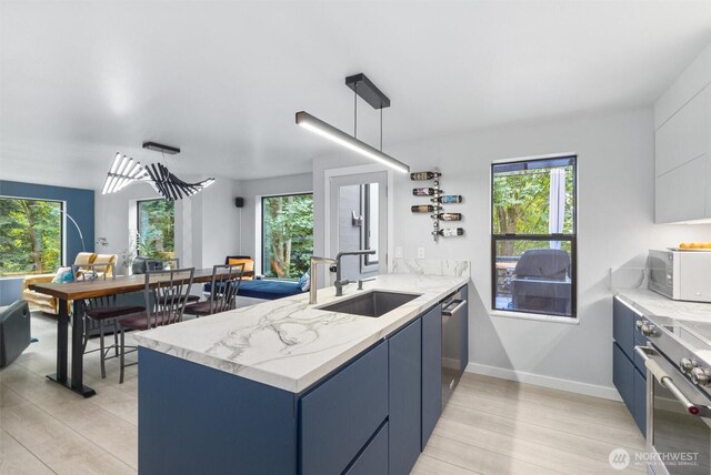 kitchen with a sink, white microwave, a peninsula, blue cabinetry, and light wood finished floors