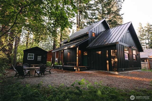 rear view of house with board and batten siding, an outdoor fire pit, metal roof, and a standing seam roof