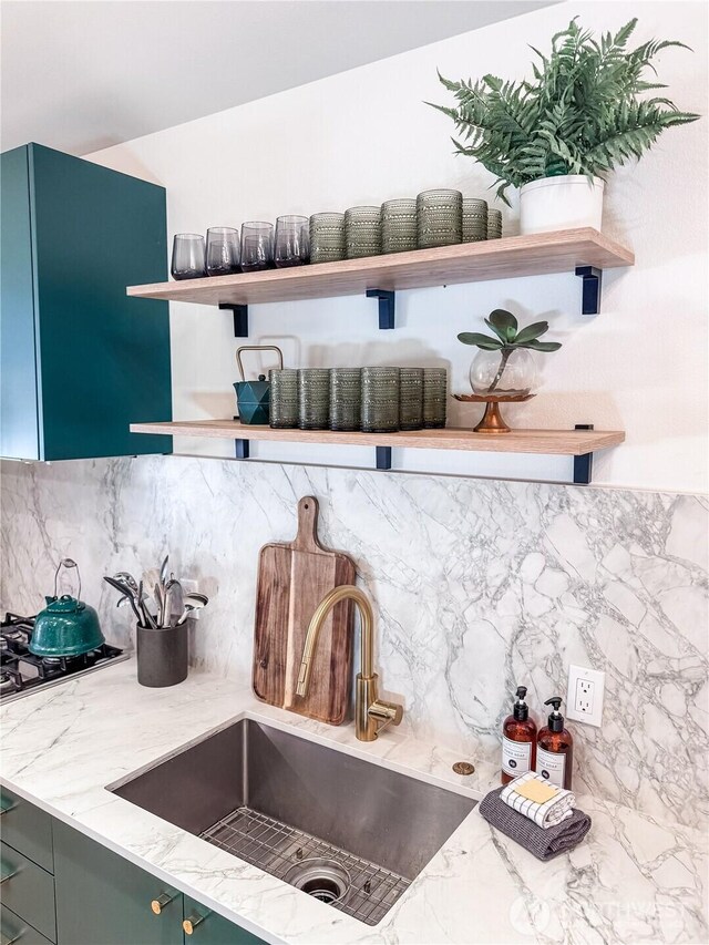 kitchen featuring open shelves, a sink, light stone counters, and backsplash