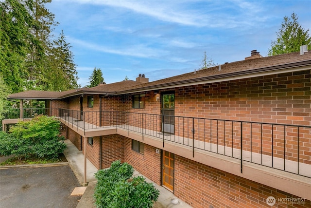 view of side of home with a balcony, brick siding, an attached garage, and a chimney