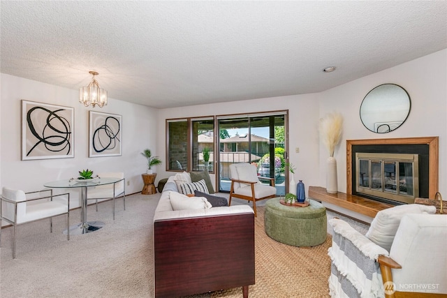 living room with a textured ceiling, carpet floors, a chandelier, and a glass covered fireplace
