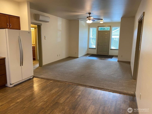 foyer with a wall unit AC, baseboards, dark colored carpet, ceiling fan, and dark wood-type flooring