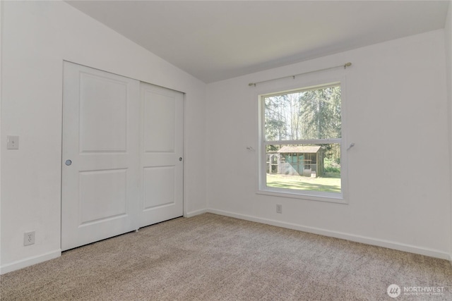unfurnished bedroom featuring carpet floors, lofted ceiling, baseboards, and a closet