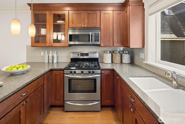 kitchen with stainless steel appliances, a sink, brown cabinetry, and light stone countertops