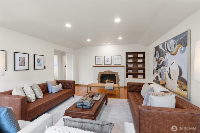 living area featuring a stone fireplace, wood finished floors, vaulted ceiling, and recessed lighting