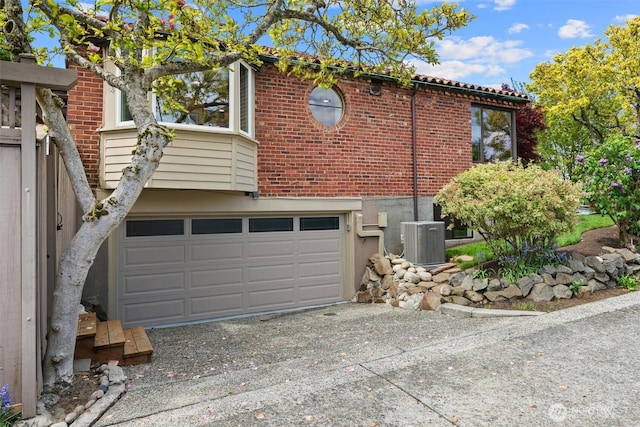 view of side of home with central air condition unit, driveway, brick siding, and an attached garage