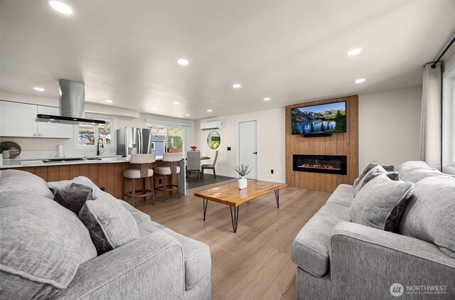 living area featuring a wall unit AC, recessed lighting, light wood finished floors, and a fireplace
